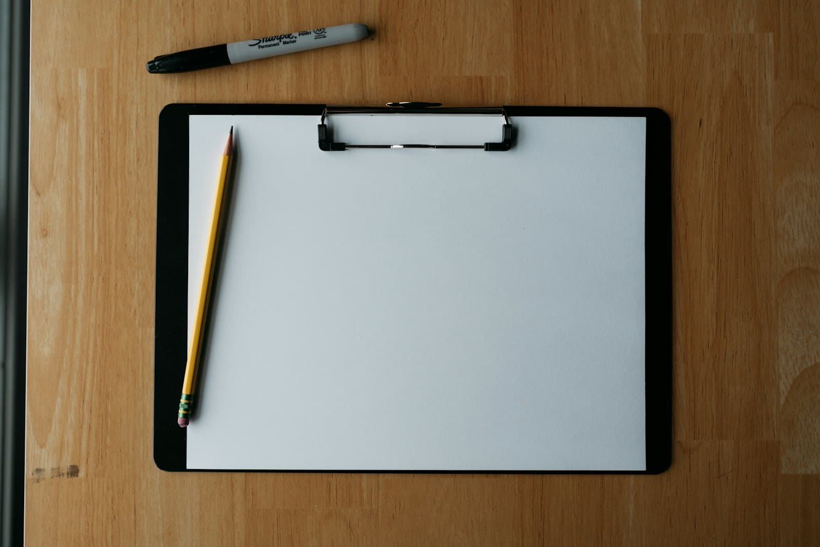 A clipboard, pencil and marker on a desk